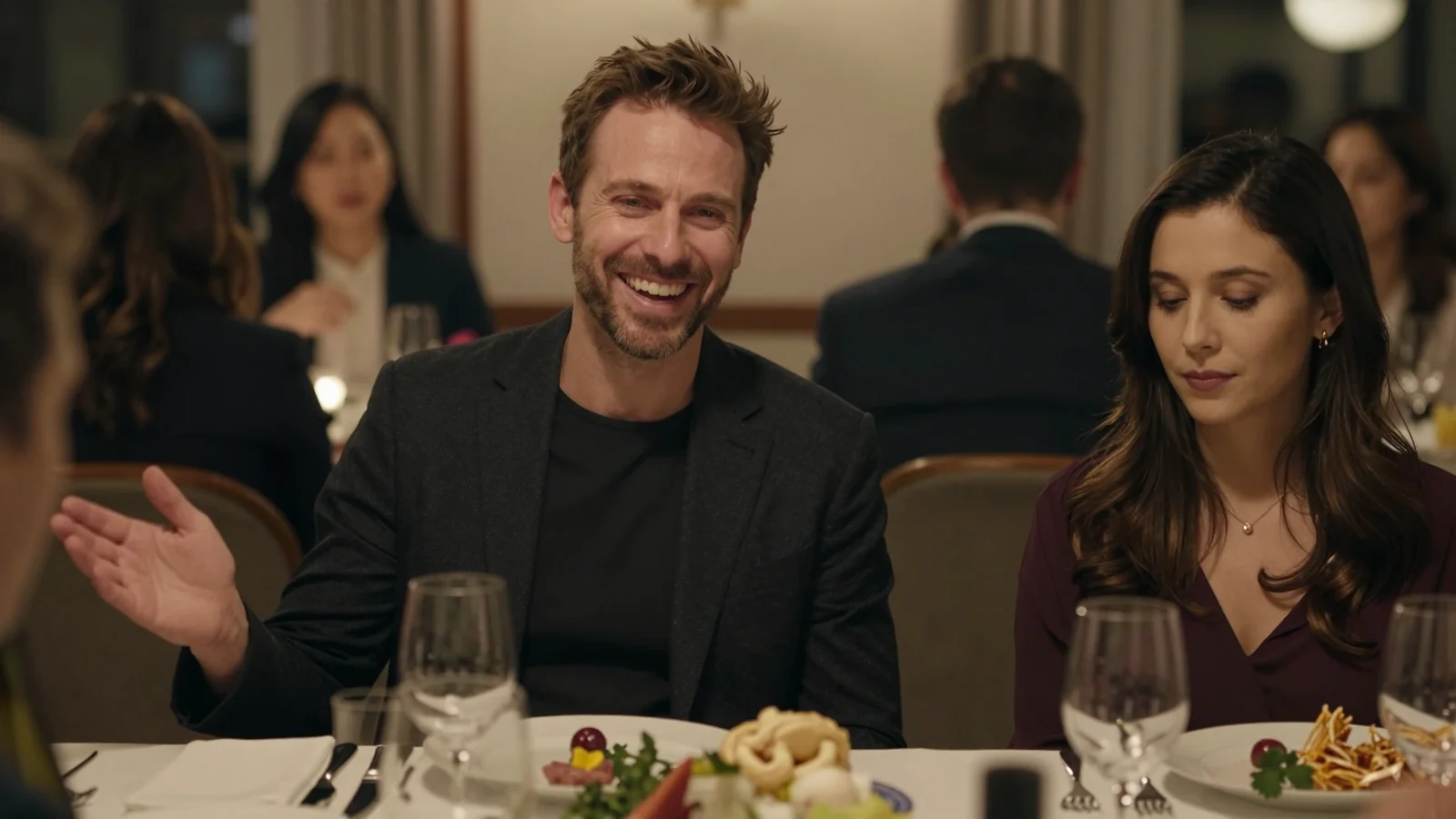 Homme souriant et charmant en société à table, femme à ses côtés le regard baissé, effacée