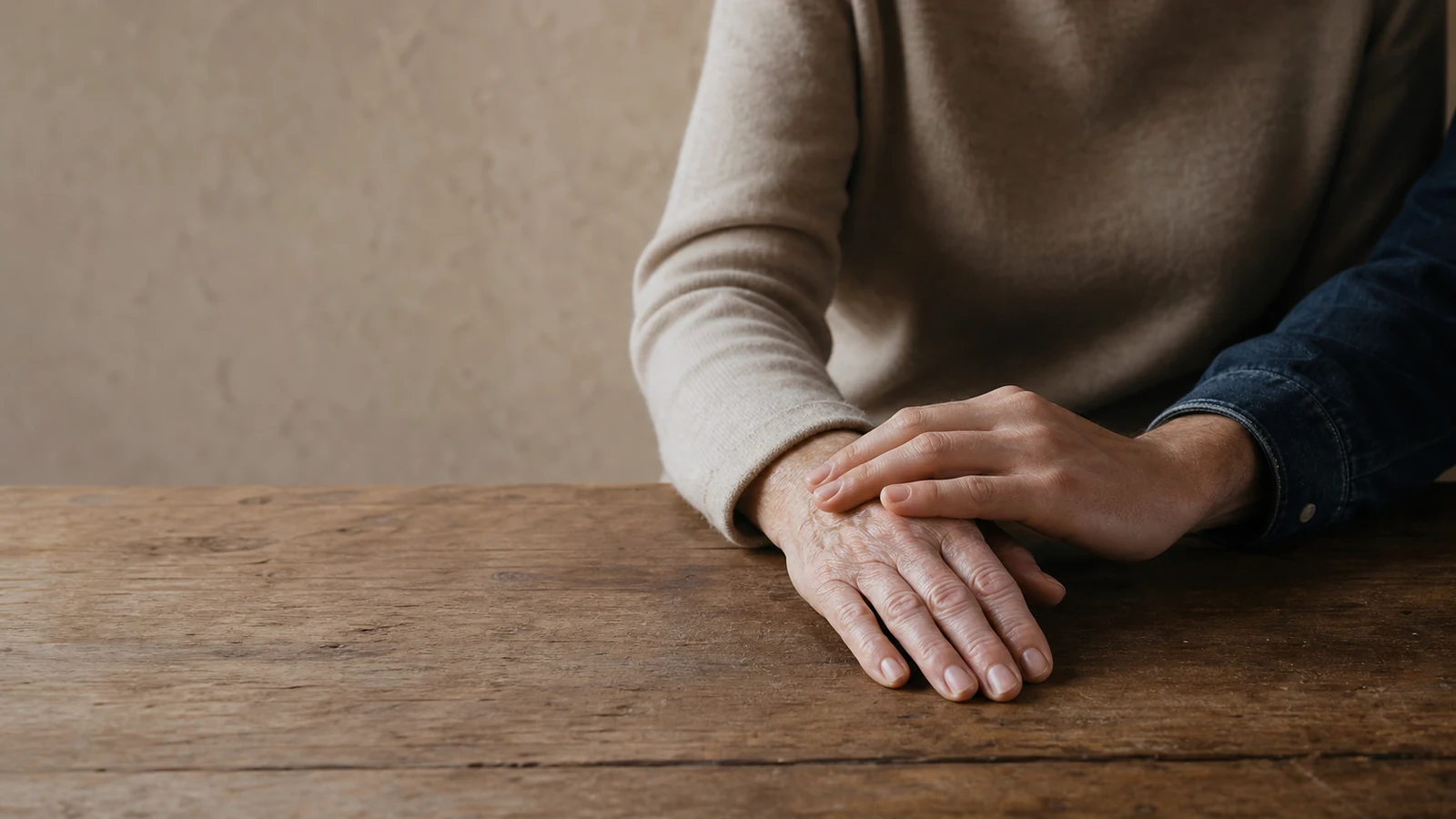 Deux mains d’âges différents se touchent sur une table en bois, dans une lumière douce.